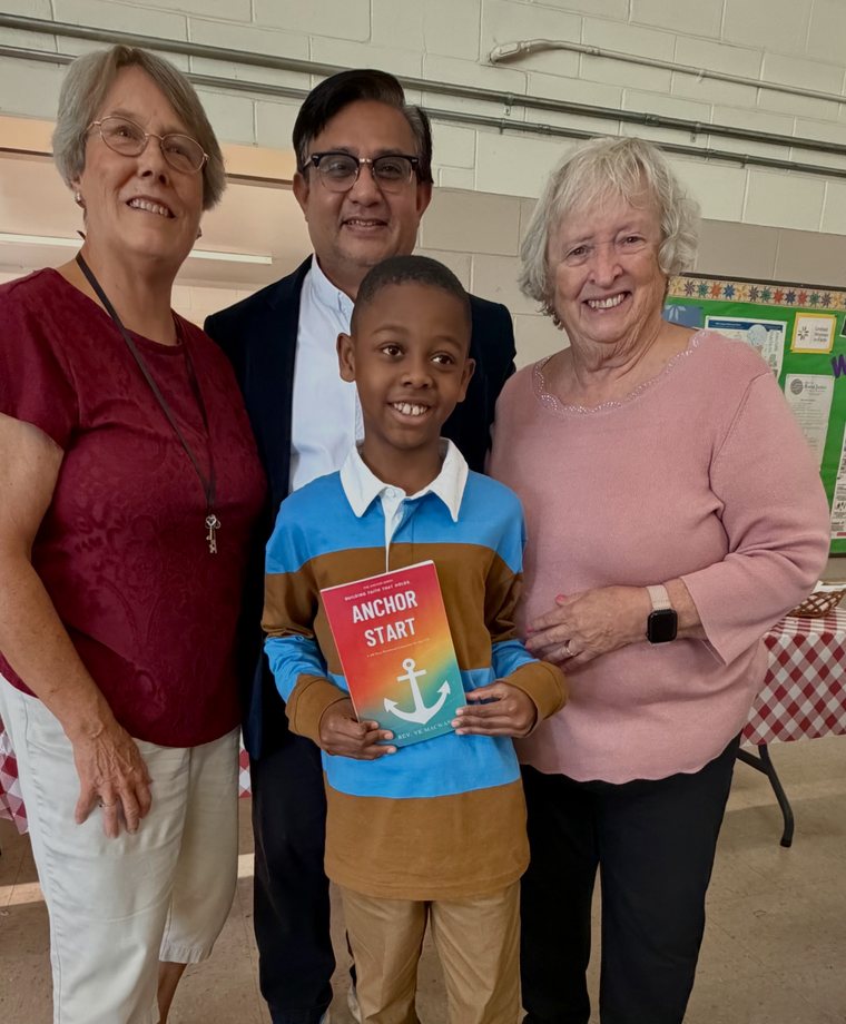 A young reader holding his signed copy of Anchor Start with the youth group leaders at Morrisville UMC